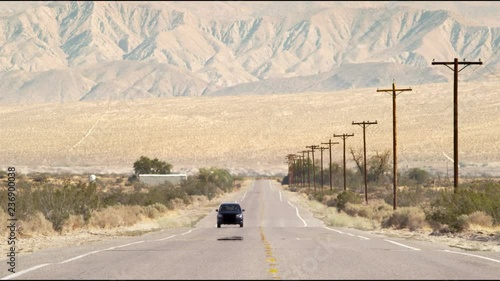 Car driving down hot desert road with mountain background