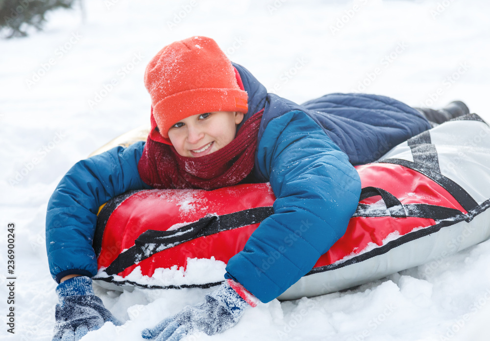 Tablet experimental Sorrow Happy teenage boy sliding down hill on snow tube laughing and showing  excitement while he slides downhill. Snow tubing on winter day outdoors.  Winter activity, leisure and entertainment concept Stock Photo 