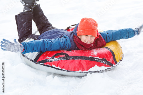 Happy teenage boy sliding down hill on snow tube laughing and showing excitement while he slides downhill. Snow tubing on winter day outdoors. Winter activity, leisure and entertainment concept