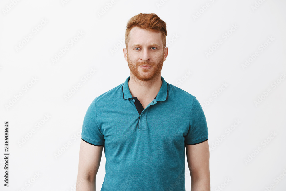Waist-up shot of attractive masculine macho man with ginger hair in green polo shirt smirking and gazing with confident and self-assured expression at camera, feeling calm and ready to work Waist-up shot of attractive masculine macho man with ginger hair in green polo shirt smirking and gazing with confident and self-assured expression at camera, feeling calm and ready to work