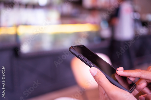 Woman hand using smartphone and laptop with cafe shop sunlight shade to object beautiful background.