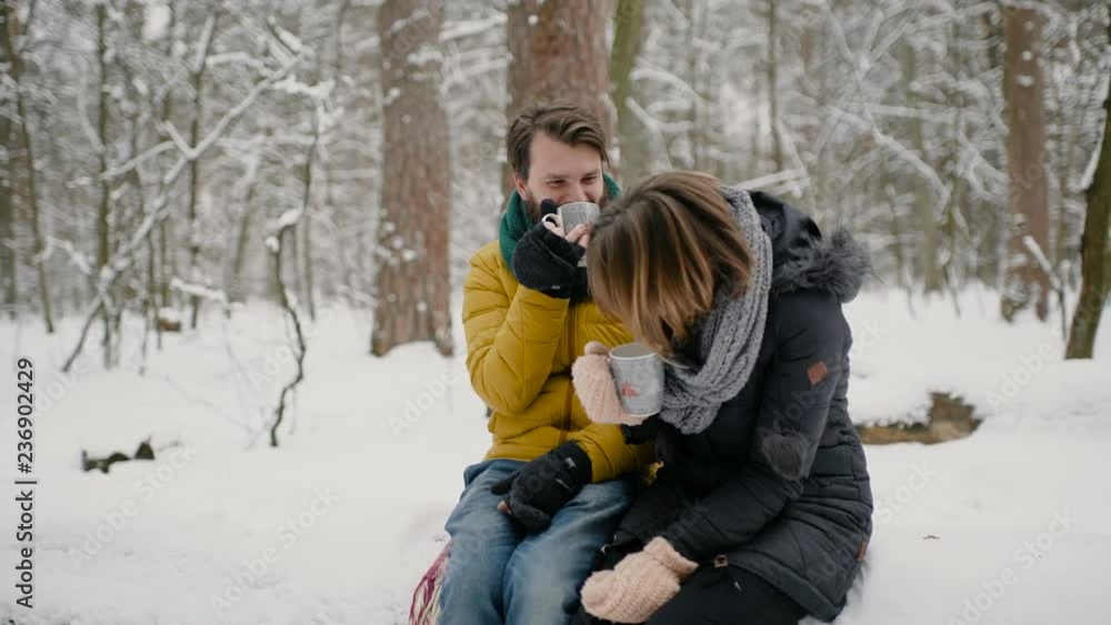 A boy and a girl, dressed in warm winter clothes, enjoy each other's presence in a snowy winter park, warming each other, and drinking a hot drink. 4к. A boy and a girl, dressed in warm winter clothes, enjoy each other's presence in a snowy winter park, warming each other, and drinking a hot drink. 4к.