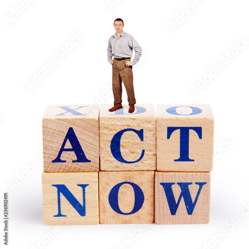 Adult caucasian man stands upon a heap of wooden blocks with a call Act Now photo