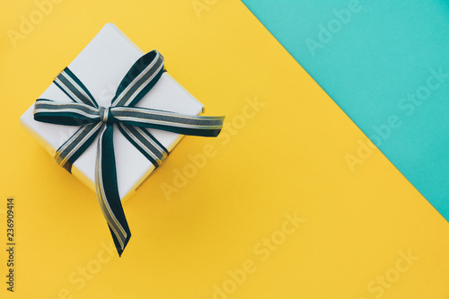 white wrapped gift present box decorated with ribbon bows on yellow and green paper texture background, copy space, top view, new year, holidays and celebration concept © iamtui7