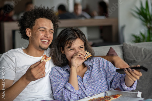 Happy couple watching tv while eating pizza. Shallow depth of field, focus on the man