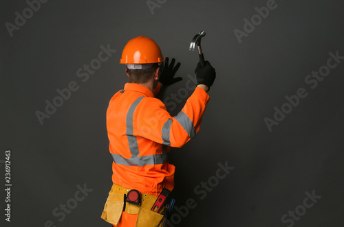Slika na platnu Builder worker is hammering a nail into the wall by the hammer in his hand