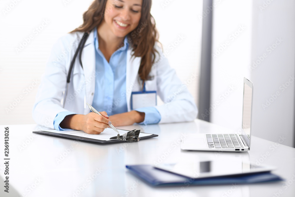 Unknown doctor woman filling up medical form while sitting at the desk in hospital office. Physician at work. Medicine and health care concept Unknown doctor woman filling up medical form while sitting at the desk in hospital office. Physician at work. Medicine and health care concept