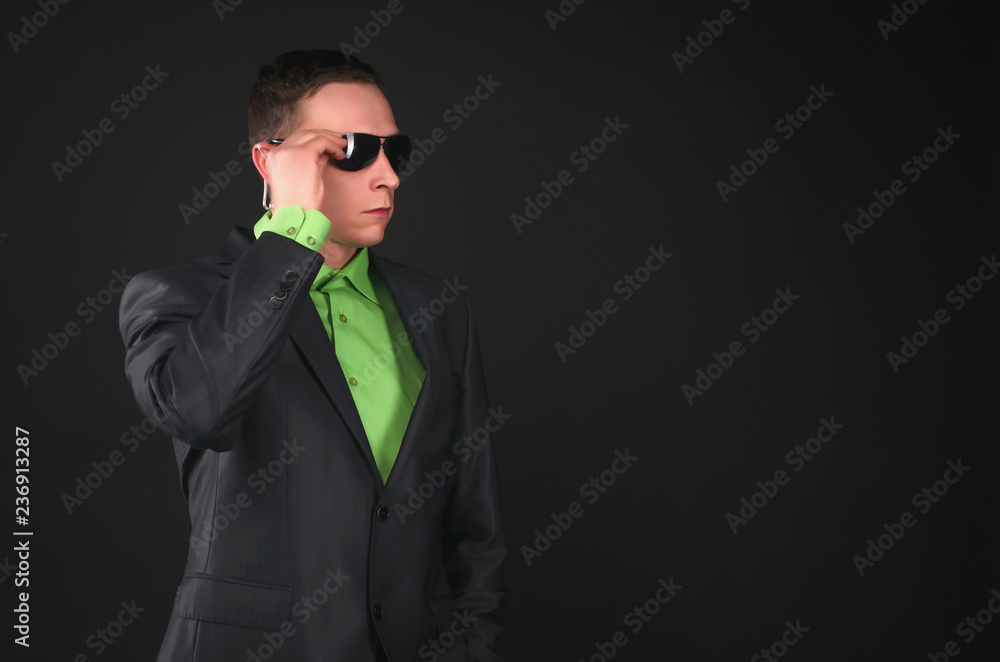 Security agent man in sunglasses and suit and with portable radio in his ear is intently looking forward isolated on black background. Security agent man in sunglasses and suit and with portable radio in his ear is intently looking forward isolated on black background.