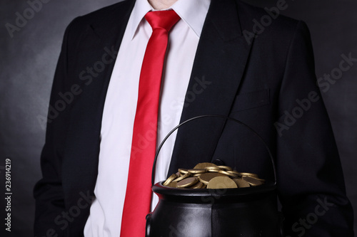 A man wearing a black suit is holding a pot of gold photo