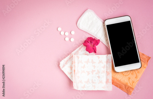 Woman hygiene protection. Sanitary pads with pain pill, pink rose and mobile phone on pink background. Menstrual cycle tracking. photo