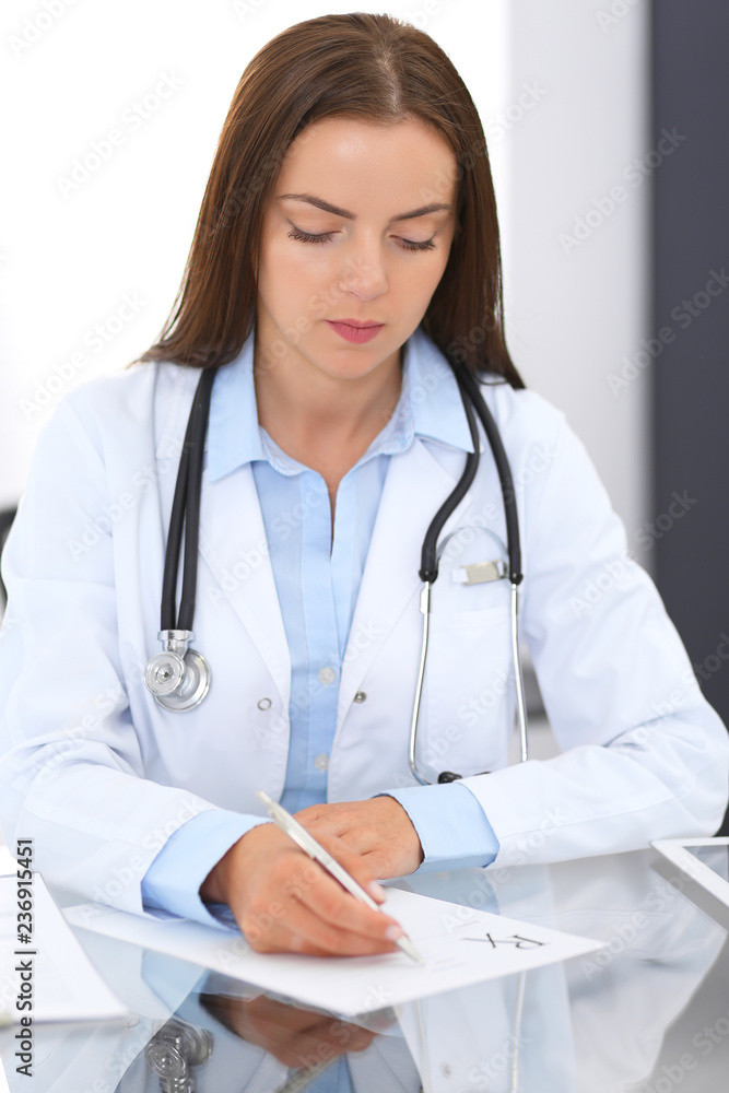 Doctor woman at work. Portrait of female physician filling up medical form while sitting at the glass desk at clinic or hospital. Medicine and healthcare concept Doctor woman at work. Portrait of female physician filling up medical form while sitting at the glass desk at clinic or hospital. Medicine and healthcare concept