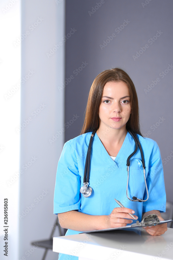 Doctor woman at work. Portrait of female physician filling up medical form while standing near reception desk at clinic or emergency hospital. Medicine and healthcare concept Doctor woman at work. Portrait of female physician filling up medical form while standing near reception desk at clinic or emergency hospital. Medicine and healthcare concept