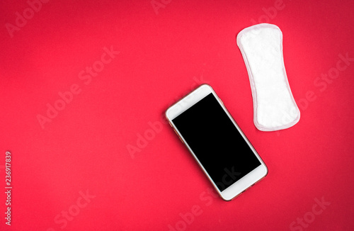 Woman hygiene protection or sanitary pads with rose petals and mobile phone on red background. Menstrual cycle tracking. photo