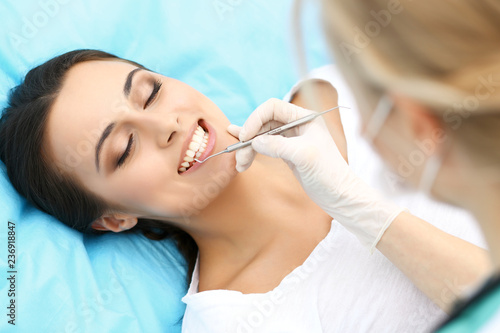 Young female patient visiting dentist office.Beautiful woman with healthy straight white teeth sitting at dental chair with open mouth during oral checkup while doctor working at teeth