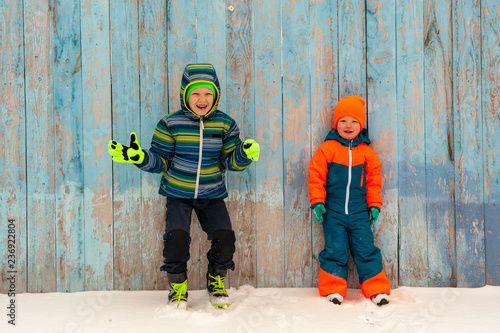 Happy children in winter warm clothes run through snow on eve in village yard. Fence with peeling paint, rustic fun, the joy of  brothers. Children are happy on vacation in the country © galitsin