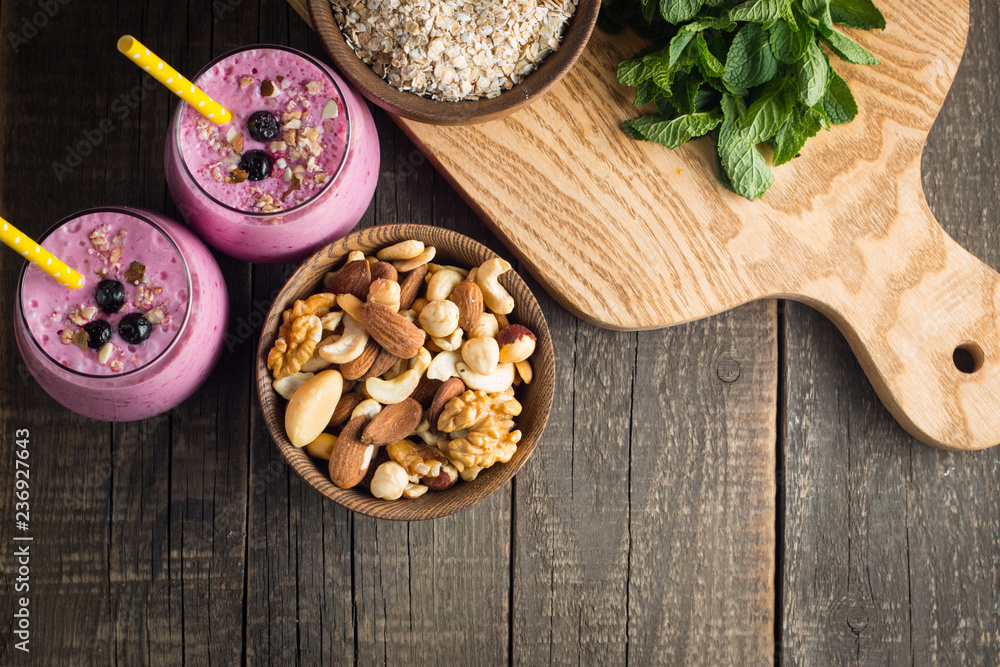 Fototapeta premium Glasses of berry smoothie with nuts, mint, blueberry, blackberry, raspberry, and yogurt on wooden table. Weight loss and diet concept. 