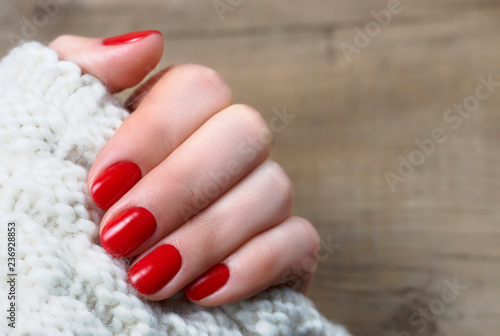 Fotografie Female hand with red manicure on a white knitted background with copy space, top