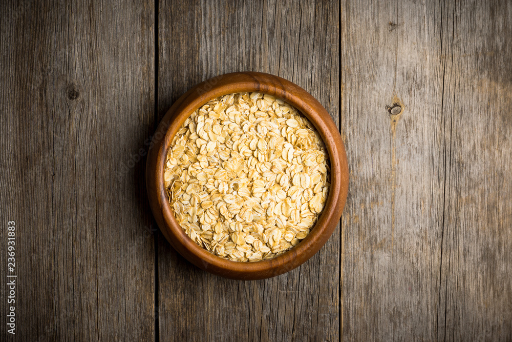 Wooden bowl with uncooked oats on the rustic wooden background. Selective focus. Shallow depth of field. Wooden bowl with uncooked oats on the rustic wooden background. Selective focus. Shallow depth of field.
