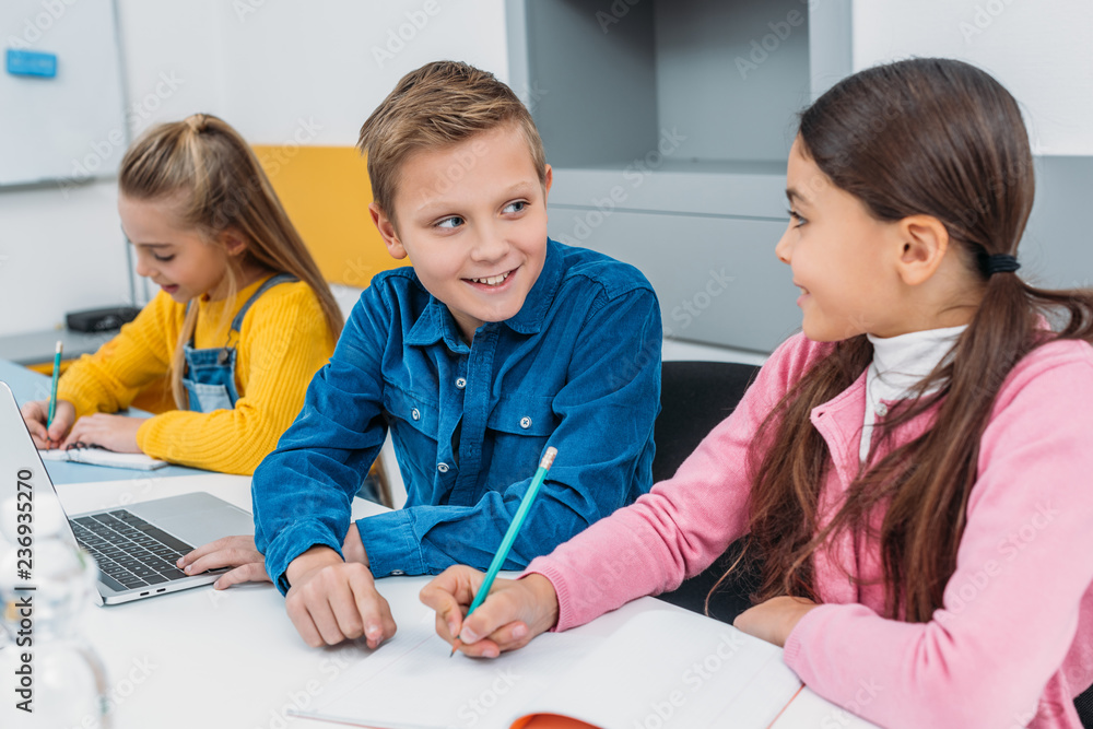 smiling children sitting at desk and in modern classroom smiling children sitting at desk and in modern classroom