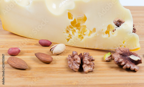 Piece of maasdam cheese among of various nuts close-up