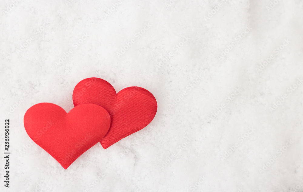 Two decorative red hearts are on white snow background with copy space for message.