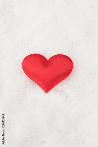Vertical image of red heart is on white snow background. Concept: love.