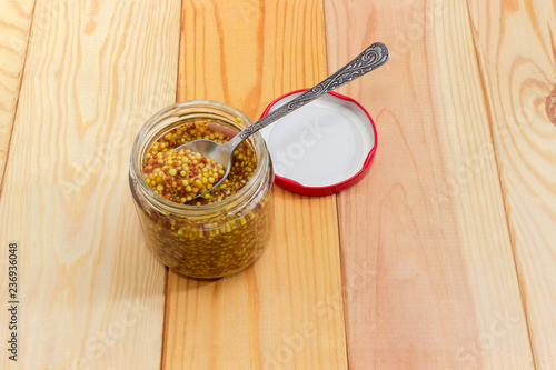 French mustard on spoon in glass jar on wooden surface
