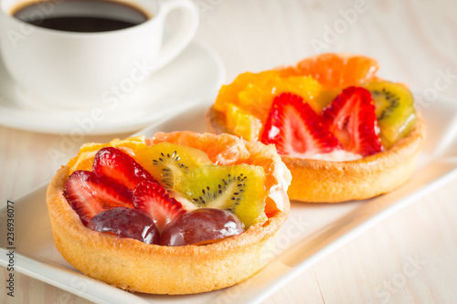 Photo of a fruit and berry tart dessert with toss sugar on wooden background. Fresh delicious sweet cake with raspberries, grapes, strawberries, cherry, kiwi, grapefruit and cream.