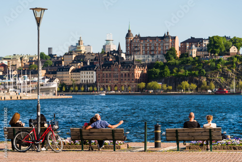 Stockholm cityscape. People relax on a benches along embankment. City break in a summer sunny day