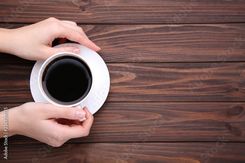 Female hands holding cup of coffee on brown wooden background.