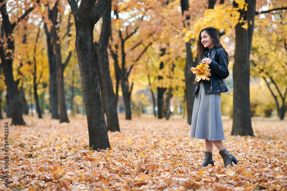Pretty woman is posing with bunch of maple's leaves in autumn park. Beautiful landscape at fall season. Pretty woman is posing with bunch of maple's leaves in autumn park. Beautiful landscape at fall season.