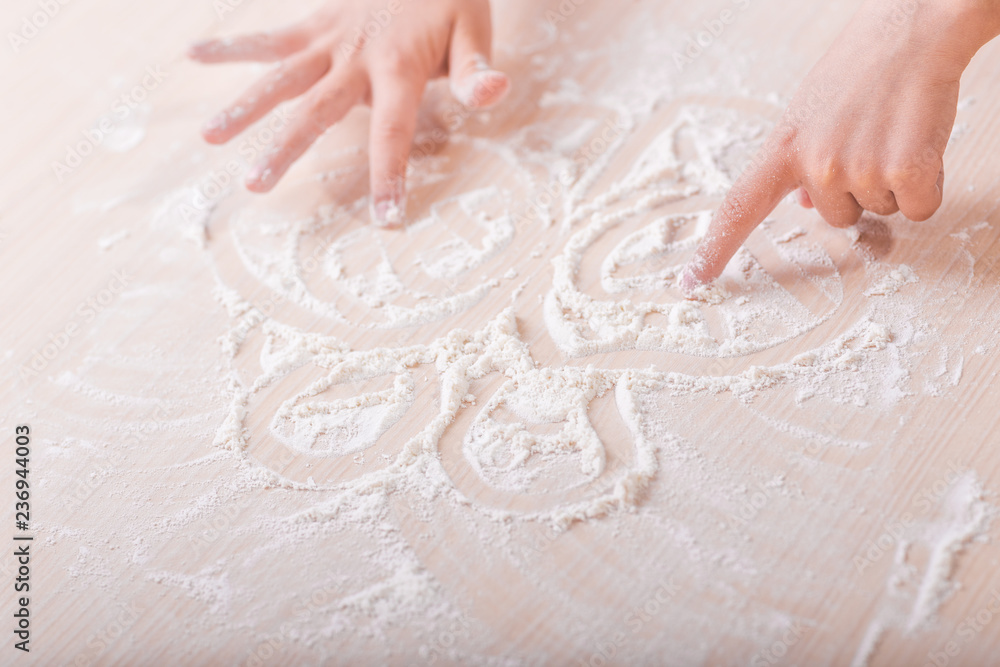 Obraz premium children's hands draw patterns of white flour on the table. baking preparation stage. little game