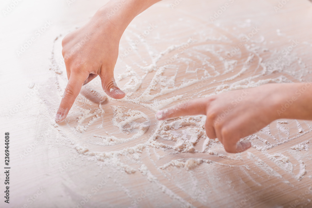 Fototapeta premium children's hands draw patterns of white flour on the table. baking preparation stage. little game