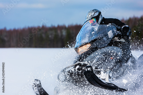 In deep snowdrift snowmobile rider driving fast. Riding with fun in white snow powder during backcountry tour. Extreme sport adventure, outdoor activity during winter holiday on ski mountain resort. photo