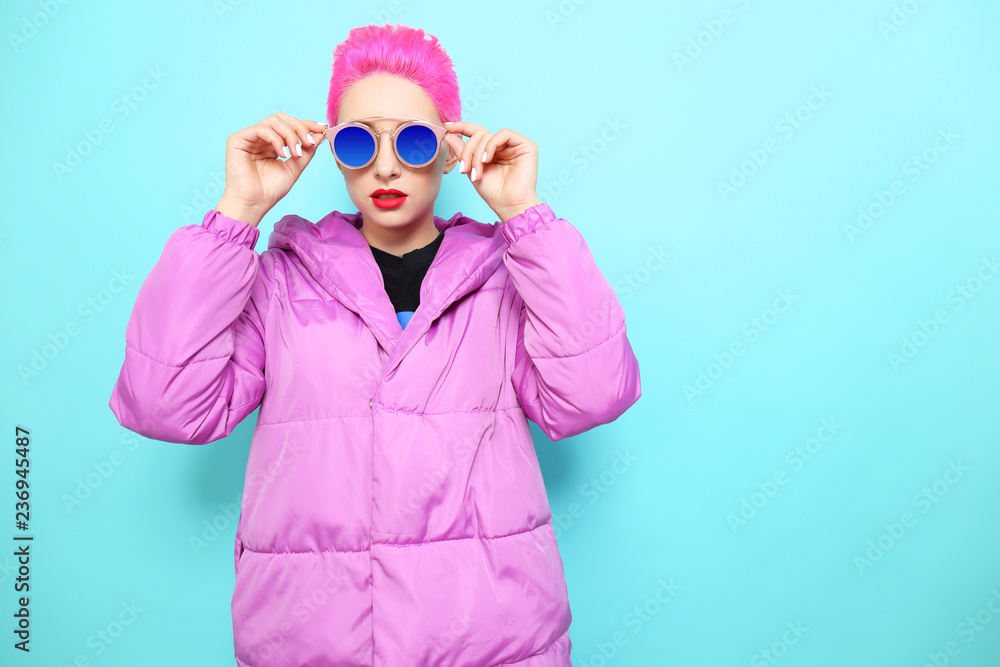 Fashion portrait of young hipster woman in lilac down jacket. Short pink hair, sunglasses, red lips, turquoise background Fashion portrait of young hipster woman in lilac down jacket. Short pink hair, sunglasses, red lips, turquoise background