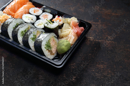 Sushi. Jedzenie na wynos. Tacka z kawałkami sushi , imbirem , wasabi i sosem sojowym na ciemnym tle.