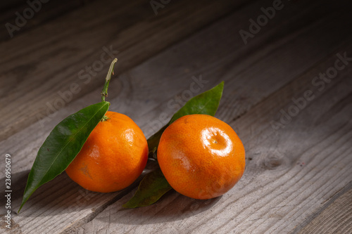 Two bright tangerines with leaves on a wooden table 