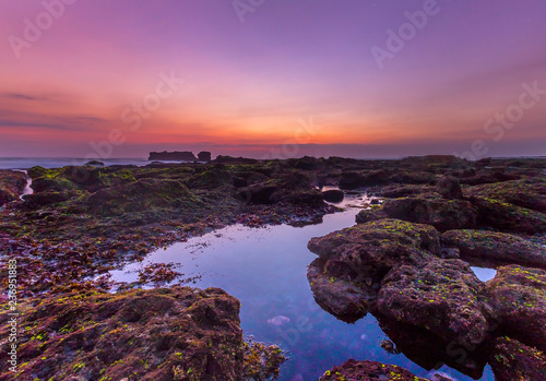 Sunset as seen from Mengening Beach, Bali,Indonesia. Mossy rocks in the foreground. Vibrant Colour and grain effects.