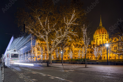 Budapest, Hungary - Festively decorated light tram (Fenyvillamos) on the move with Parliament of Hungary at Kossuth square by night. Christmas season in Budapest photo