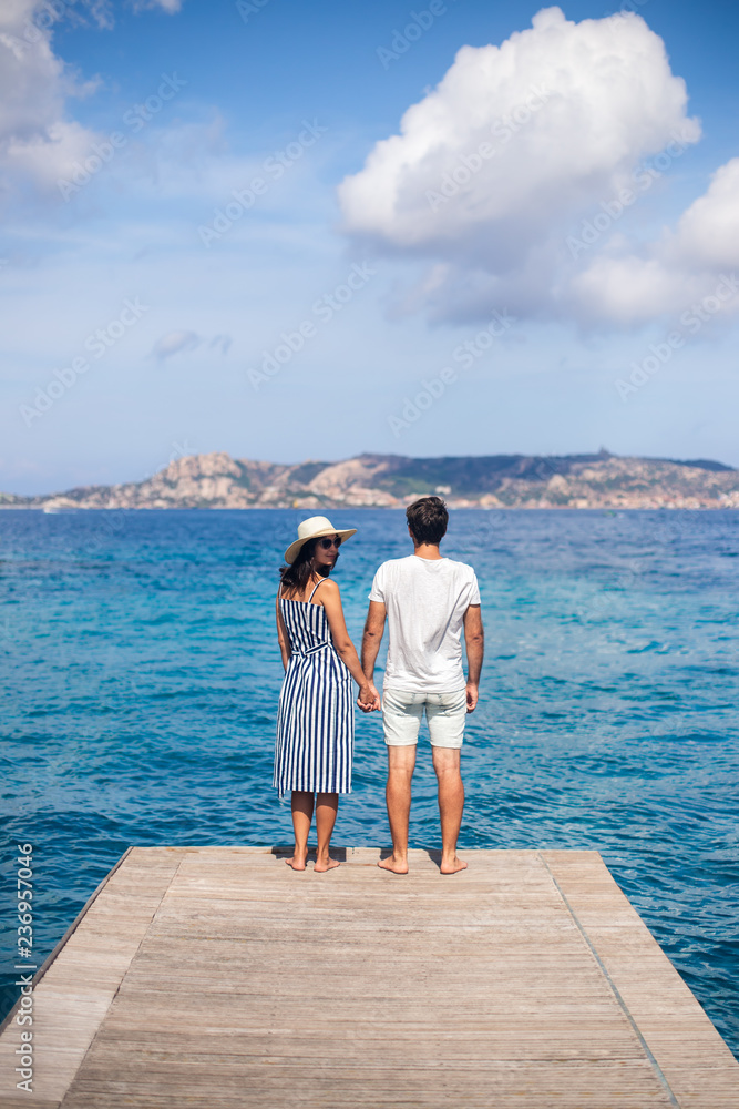 Back view of young couple in love relax on pier in Italy, woman looking to camera