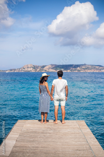 Back view of young couple in love relax on pier in Italy, woman looking to camera