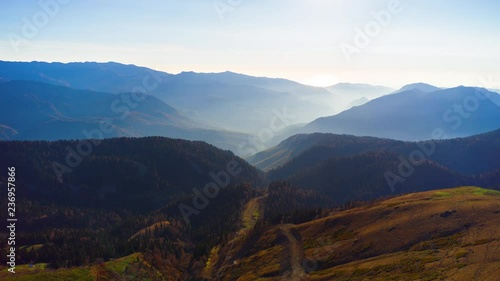 Beautiful aerial view to the evening mountains in Sochi Roza Hutor. Picturesque motion timelapse of autumn valley with the sun behind the peaks and hazy sunshine. 8K ultra high definition footage. photo