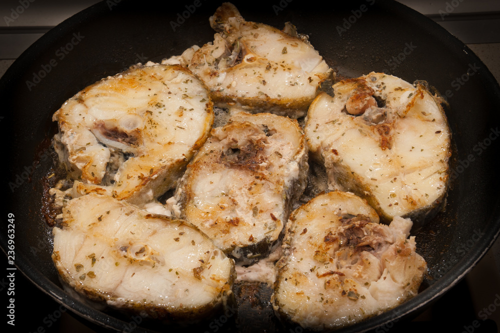 Fried cod fish in a pan with condiment and herbs