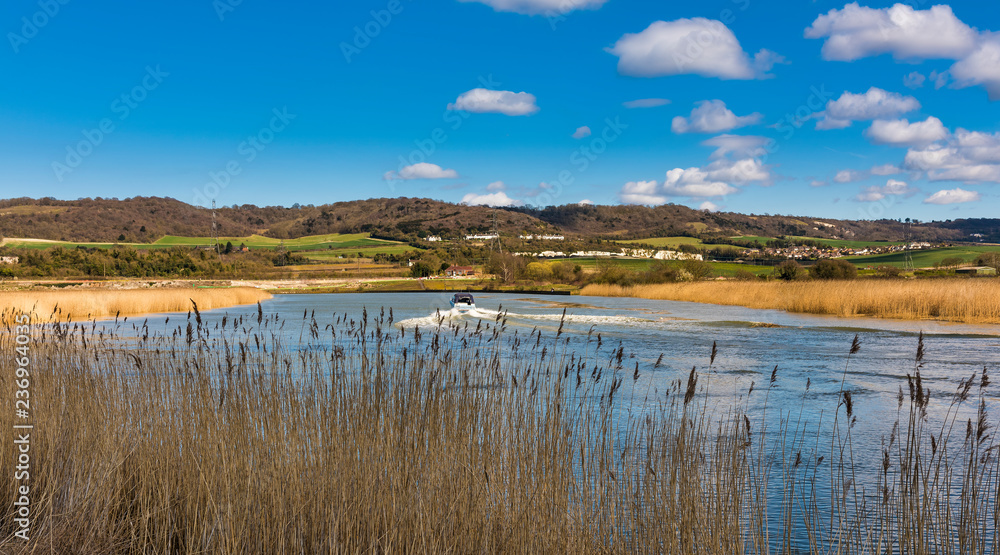View from the banks of the River Medway at Snodland near Maidstone in Kent, England on a beautiful spring afternoon. In the distance can be seen the North Downs and a boat heading towards Rochester.