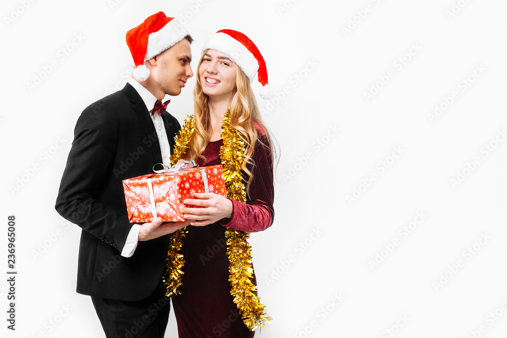 An elegant pair of lovers in Santa Claus hats celebrating the New Year and giving each other Christmas presents. An elegant pair of lovers in Santa Claus hats celebrating the New Year and giving each other Christmas presents.