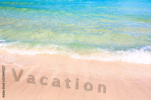 Inscription of a vacation word on the sand on beautiful beach with a blue turquoise sea wave. Concept of a summer vacation and recreation