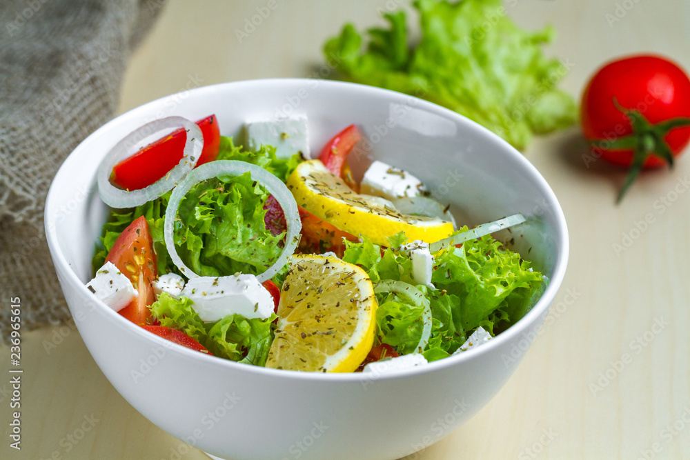 Fresh, healthy vegetable salad with lettuce, cherry tomatoes, onion, feta cheese, lemon, sprinkled with spices in a plate. Proper nutrition and right food. Diet Fresh, healthy vegetable salad with lettuce, cherry tomatoes, onion, feta cheese, lemon, sprinkled with spices in a plate. Proper nutrition and right food. Diet