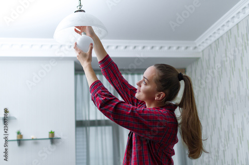 Fototapeta Naklejka Na Ścianę i Meble -  Young, attractive housewife makes the replacement of the used LED light bulb in the chandelier in the room
