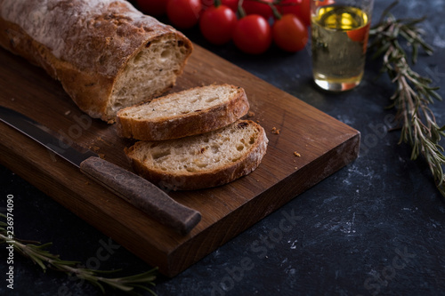 Crusty homemade ciabatta bread on wooden cutting board with tomatoes and olive oil.