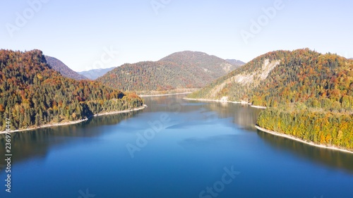 Autumn color forest, aerial view over colorful autumn trees, towards lake and on a sunny fall day